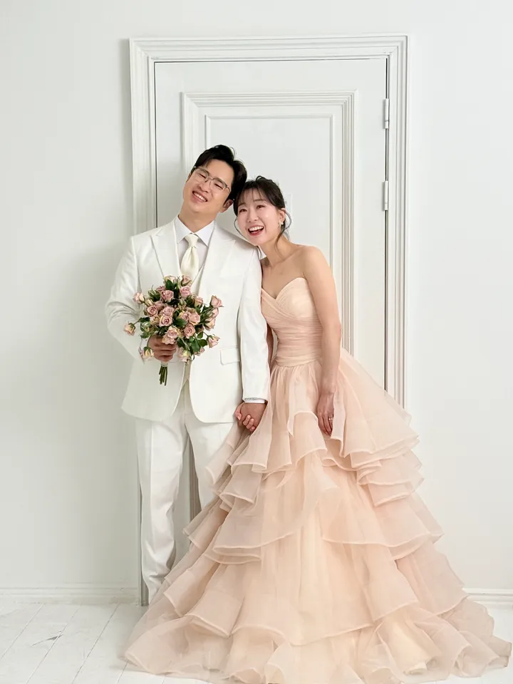 흰 문 앞에서 머리를 기댄 신랑과 피치색 드레스의 신부