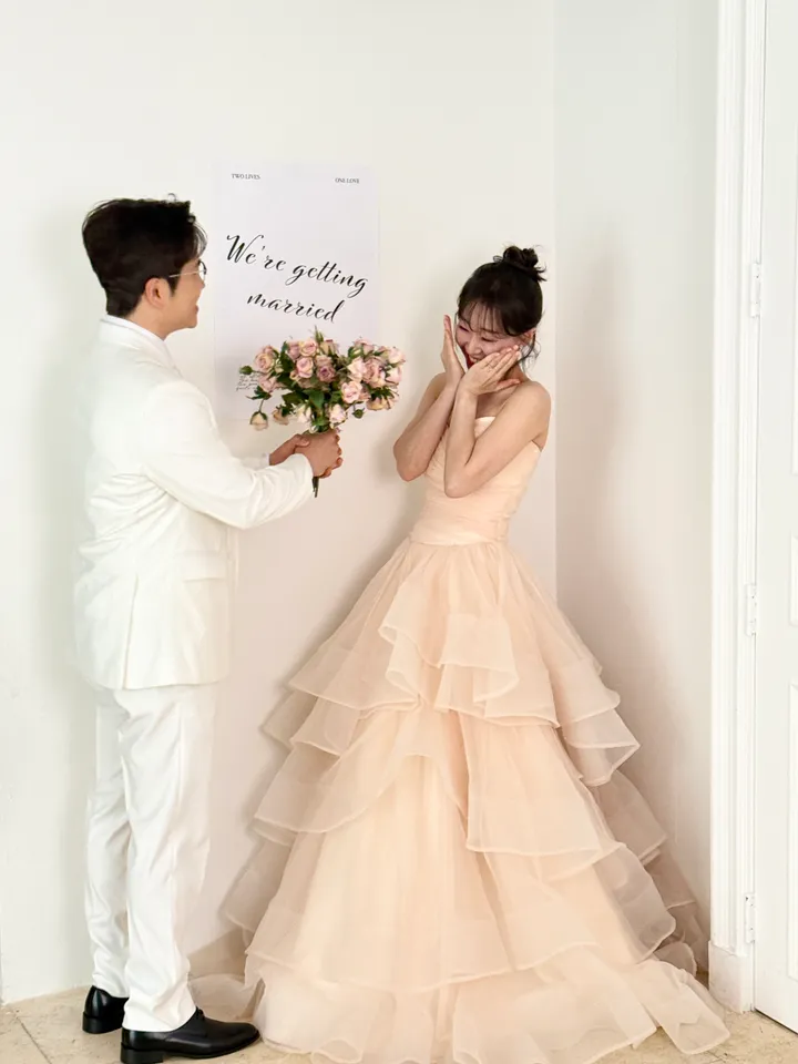 ‘We're getting married’ 문구 앞에서 꽃다발을 건네는 신랑과 놀란 신부