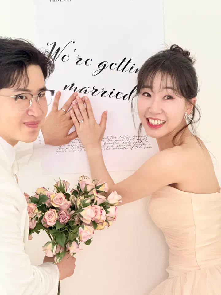 반지를 낀 두 손을 ‘We're getting married’ 문구 위에 올린 신랑과 신부