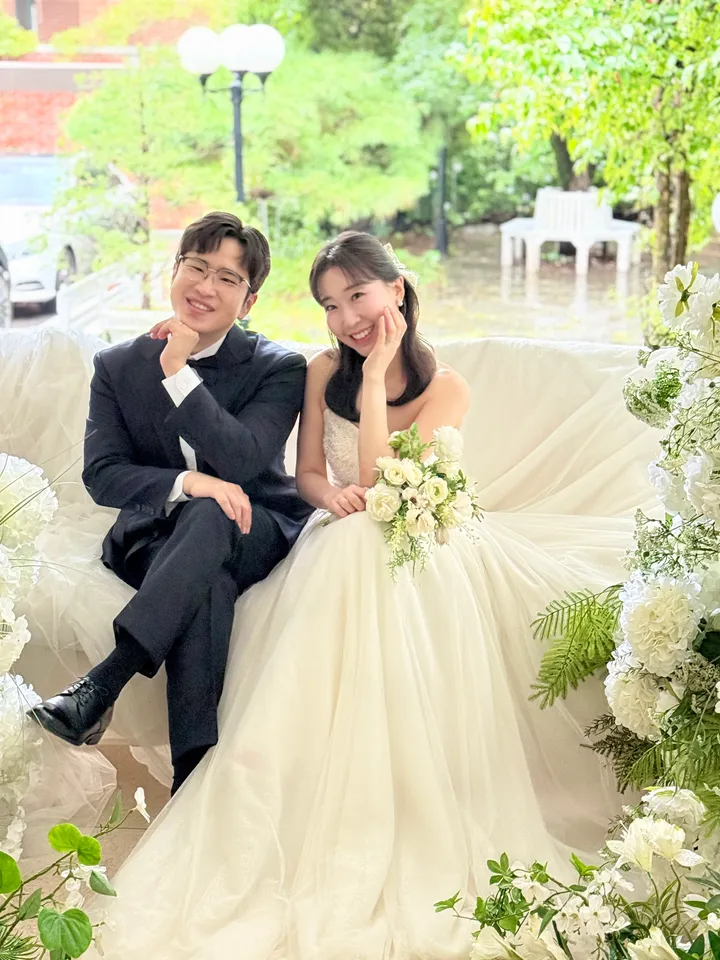 꽃으로 꾸민 정원 소파에 나란히 앉은 신랑과 신부
