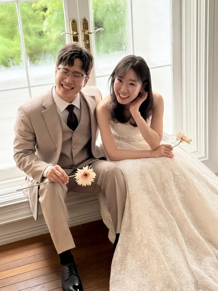 창가에 나란히 앉아 거베라를 든 신랑과 신부