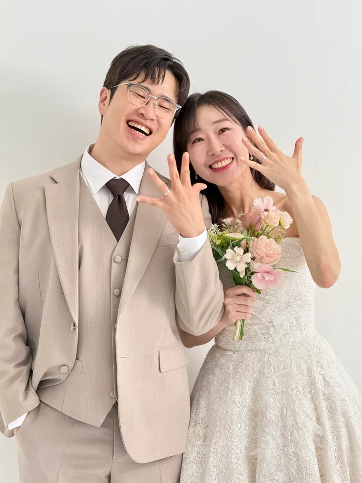 반지를 낀 손을 들어 보이며 웃는 신랑과 신부