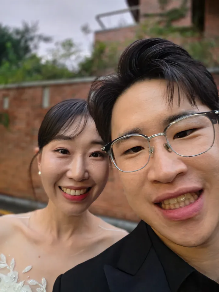 벽돌 건물 앞에서 얼굴을 가까이 대고 웃는 신랑과 신부