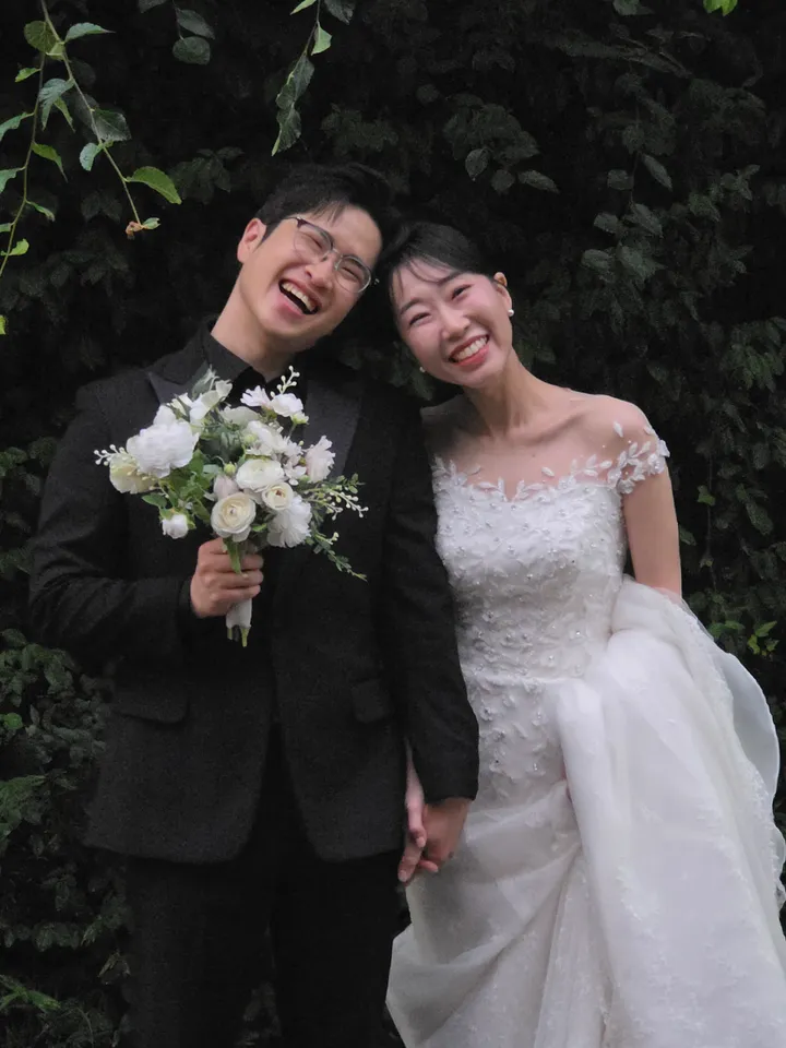꽃다발을 든 신랑과 신부가 머리를 맞대고 웃는 모습